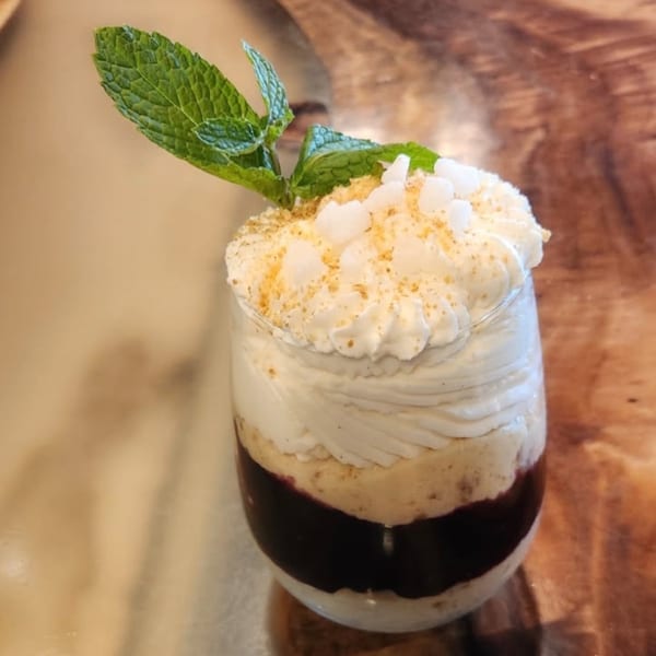 Layered dessert in a glass with whipped cream, mint, and sprinkles on a wooden table.