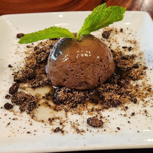 A chocolate dessert with mint leaves and cookie crumbles on a white plate at The Library On Fern.