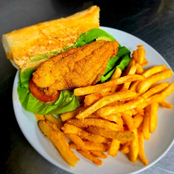 A fried fish sandwich with lettuce and tomato, served with a side of golden french fries.