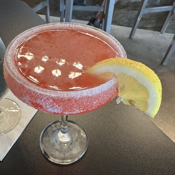 A vibrant red cocktail with a sugared rim and a lemon slice, on a dark table.